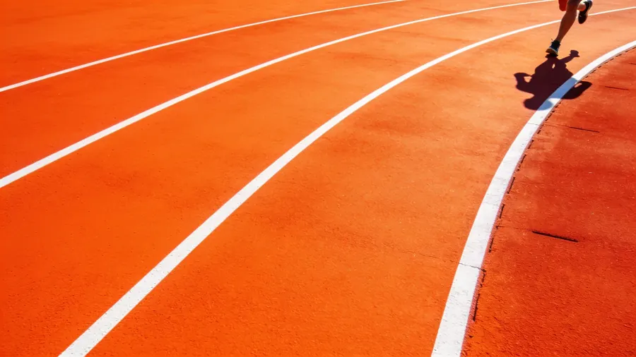 A bright orange running track photographed from directly overhead, with a runner's legs entering the frame mid-stride.